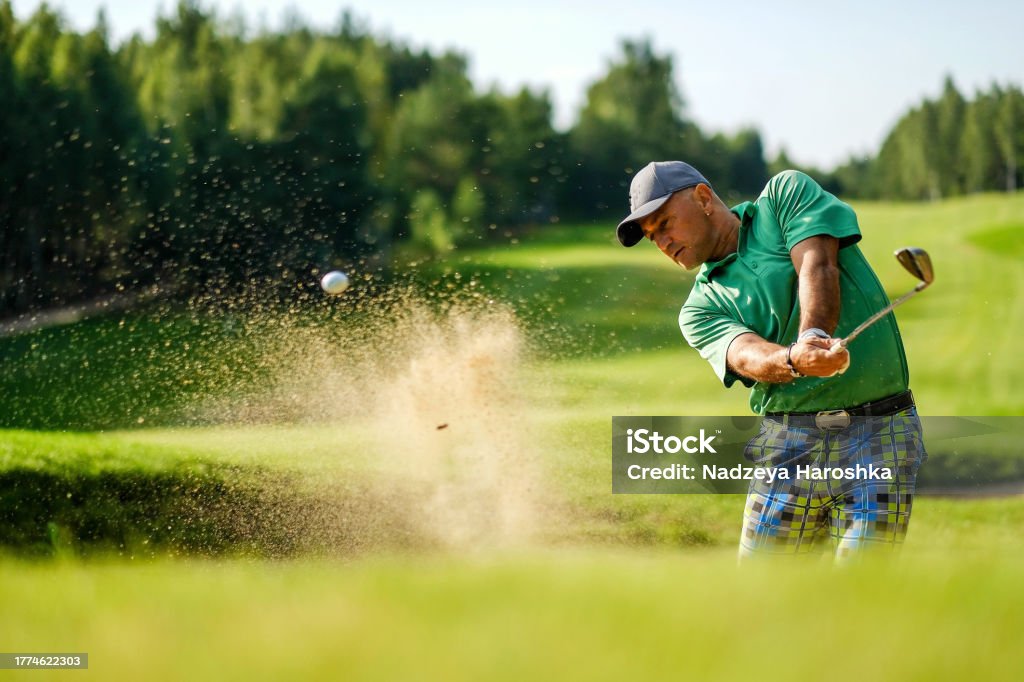 Golfista golpea la pelota desde un búnker con un palo de golf - Foto de stock de Golf libre de derechos Golfista golpea la pelota desde un búnker con un palo de golf - Foto de stock de Golf libre de derechos