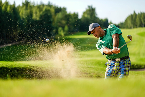Golfer hits ball from a bunker with golf club. Golfer playing golf