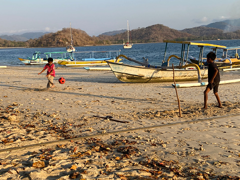 Gili Asahan, small island located southwest of Lombok Island , fisherman village and few resorts , travel boats aerial view. Boy playing  soccer on the beach at sunset