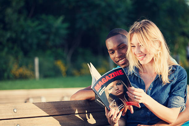 Smiling couple reading magazine in park stock photo