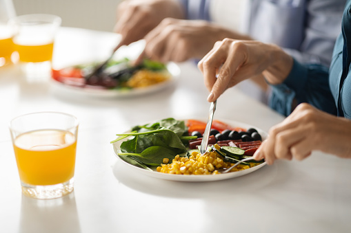 Healthy Meal. Man And Woman Eating Tasty Food In Kitchen, Unrecognizable Couple Sitting At Table And Having Vegetables And Sausages For Breakfast Or Lunch, Using Forks And Knifes, Closeup Shot