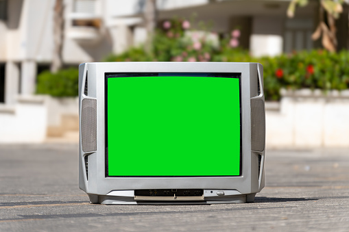 Old plastic silver coloured TV set stands on the pavement of the city street in summer. Green screen. Chromakey. Mockup