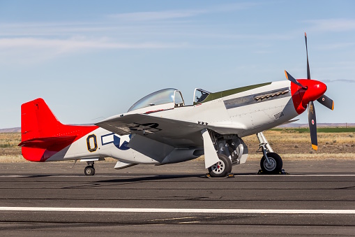 A beautifully restored North American P-51D Mustang parked on the ramp at the Grant County Airport in Moses Lake, WA.   It was the morning of a sunny, summer day and the lighting was perfect.  The brilliant red nose spinner and tail are rich in color and immediately grab the viewers attention while the pearl white body paint perfectly contrasts the red color.   This is a classic warbird and truly an iconic fighter of WWII.