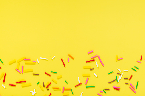 flat lay of colorful sprinkles over yellow background, festive decoration for banner, poster, flyer, card, postcard, cover, brochure, designers, copy space.