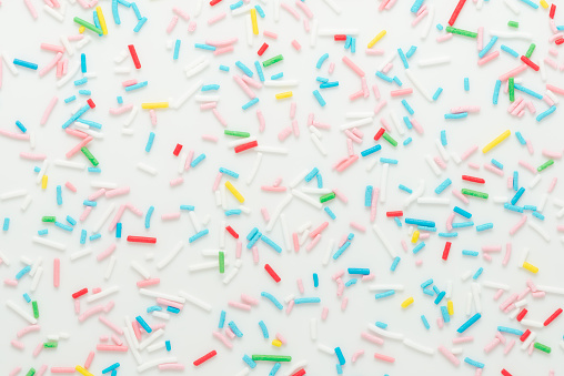 flat lay of colorful sprinkles over white background, festive decoration for banner, poster, flyer, card, postcard, cover, brochure, designers.