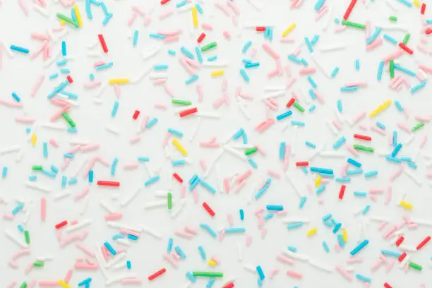 Photo of flat lay of colorful sprinkles over white background, festive decoration for banner, poster, flyer, card, postcard, cover, brochure, designers