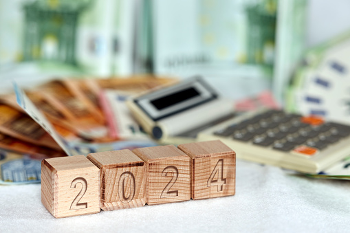 Four wooden cubes with numbers in front of a defocused calculator and green euro paper notes for Concept & Finance