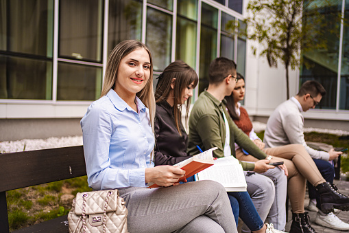 Small group of university students studying outdoors on a bench before an exam