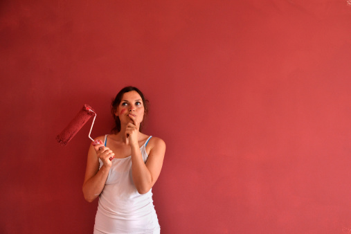 Beautiful young woman in causal clothes thinking about the result of the work she has done painting a wall with red paint and a roller