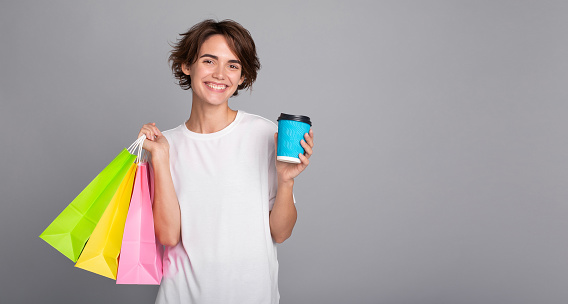 Beautiful girl with short hair holding shopping bags and paper cup in her hands. Black Friday, consumer, buyer, sale, store, payment, online buying, discount, purchase, mall, e-commerce, order, offer