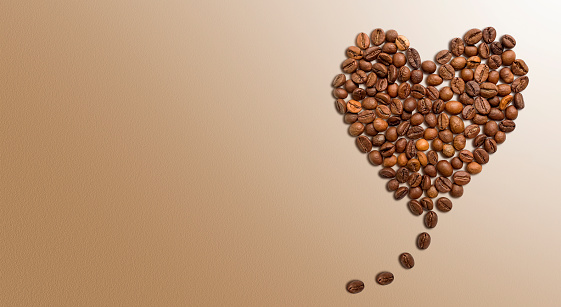 Heart shape made by roasted roasted coffee beans on a wooden background, directly above.