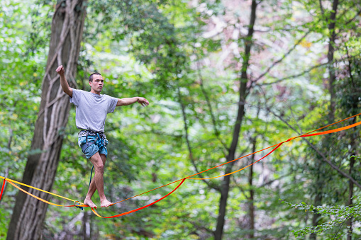 A young person walks on a highline in a green forest