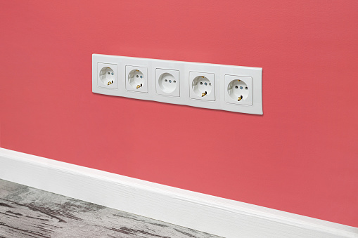 White five-way wall power socket installed on the pink wall, side view.