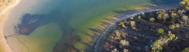 Panorama curved shoreline and remote waterfront primitive camping sites with tents at Isle du Bois Ray Roberts Lake State Park lush green tree forest near Denton, Texas, US aerial view. Adventurers