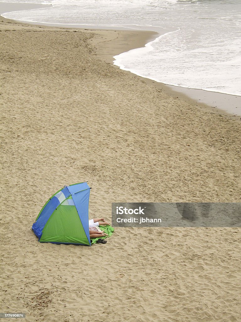 Casal dentro de uma tenda com os pés fora na praia - Foto de stock de Acampar royalty-free