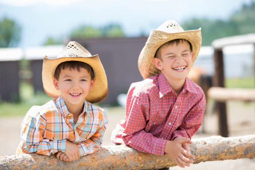 Cute little cowboys in hats leaning against fence post