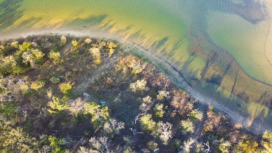 Curved shoreline and remote waterfront primitive camping sites with tents at Isle du Bois Ray Roberts Lake State Park lush green tree forest near Denton, Texas, US aerial view. Nature and adventurers