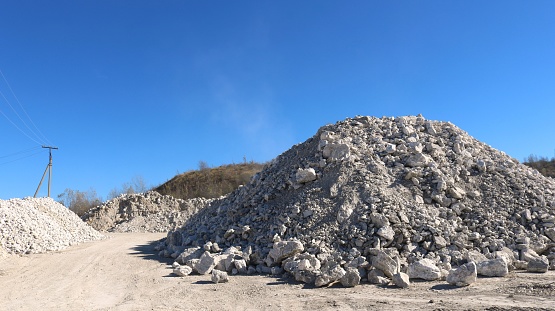 a pile of light stones in a desert landscape at a limestone mining site, a hill of white cobblestones next to a quarry, building material in the process of being extracted from the ground