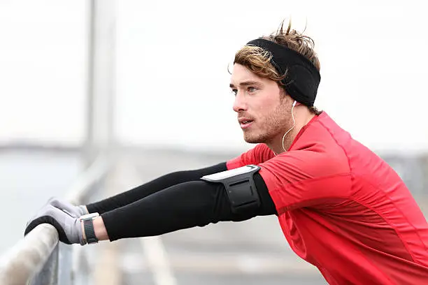 Male runner stretching after running in cold fall weather wearing warm sporty running clothing. Handsome male fitness sport model outdoors. Click for more: