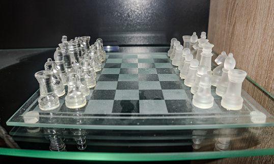 glass chess board with chess pieces. Crystal glass chess pieces on a glossy chessboard. Strategy concept. High quality photo