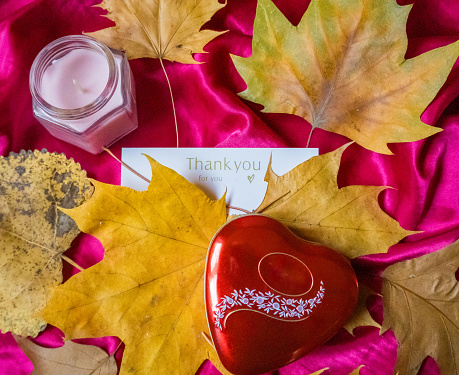 Thanksgiving. Present of Valentine on pink silk. Red heart with candle surrounded by autumn leaves . High quality photo