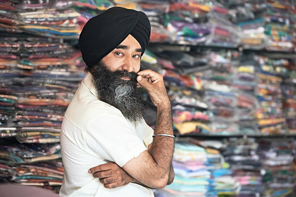 Young adult indian sikh seller man Portrait of Indian sikh man seller in turban with bushy beard at shop india indian culture market clothing stock pictures, royalty-free photos & images