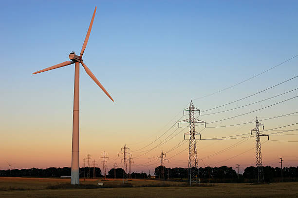 Wind turbine and electricity pylons against sky stock photo
