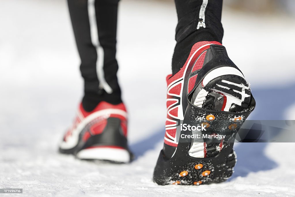 Running shoes in snow Running shoes in snow with grip soles or traction cleats with metal spikes for anti slip grip when walking or running. Man winter running in snow. Walking Stock Photo