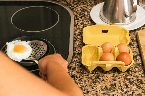 cardboard egg cup with fresh chicken eggs and hand boiling an egg in a frying pan.