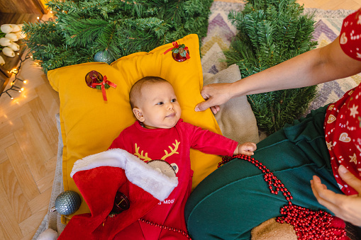 Festive decorations come to life as a mother delicately adorns the Christmas tree with her baby by her side.
