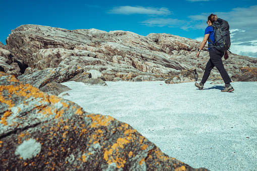Woman hiking outdoors. Adventures in summer Norway, in the Bergen area. The woman is walking on a beach made with shells fragments.