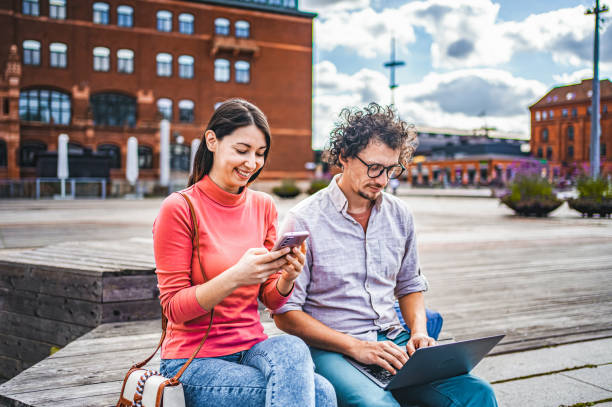 istock Two friends working together using laptop and mobile phone while sitting in the city square 1774980017