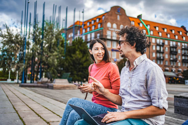 istock Two friends working together using laptop and mobile phone while sitting in the city square 1774980421