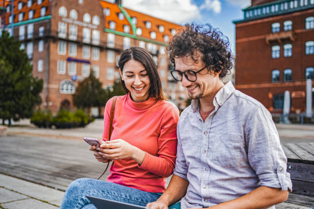 istock Two friends working together using laptop and mobile phone while sitting in the city square 1774980465