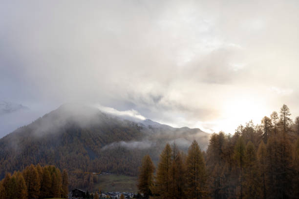 The sun rises through clouds pulling off of mountains and forested valley