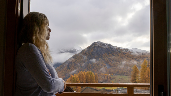 She is in a chalet above a valley and mountains with larch trees in autumn