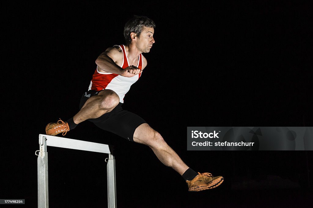 sprinter over a hurdle a sprinter is running over a hurdle in track and field Night Stock Photo