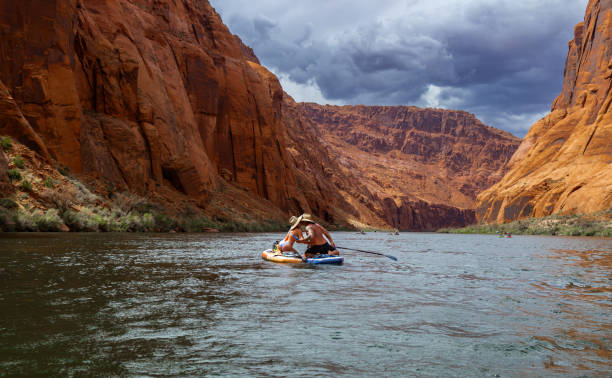 Couple explore desert lands and river together They are floating on a SUP board down a river in summertime horseshoe bend river stock pictures, royalty-free photos & images