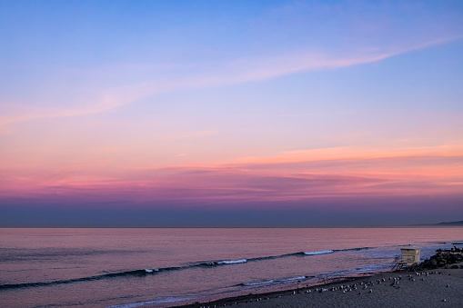 This is a beautiful sunrise photo taken early in the morning at moonlight beach California with rocks in the colorful magenta orange sand reflection of the sun asthe waves lap against the stony shore.