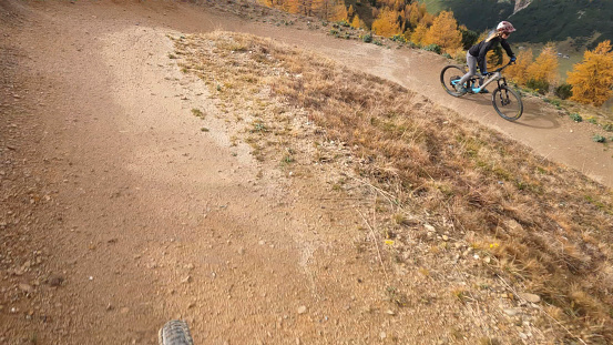 First person perspective of young woman biking down curving trail through larch forest in autumn