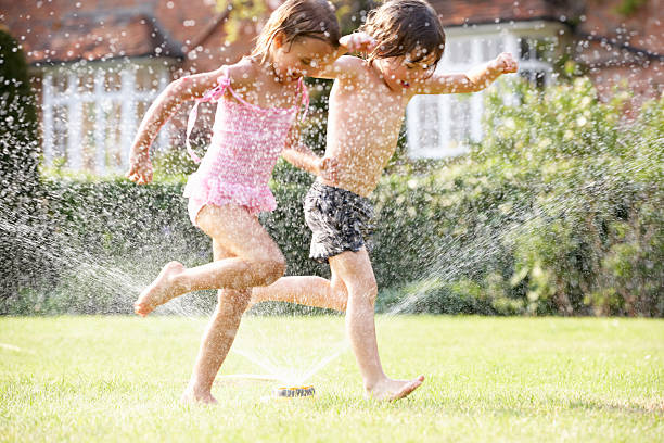 zwei kinder laufen durch den garten sprinkler - sprinkler fotos stock-fotos und bilder