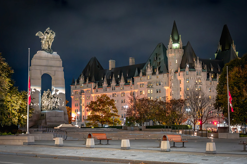 National War Memorial and Confederation Square during autumn with two National Flags at half-mast for Remembrance Day, Fairmont Chateau Laurier hotel, Ottawa, Ontario, Canada (November 2023).