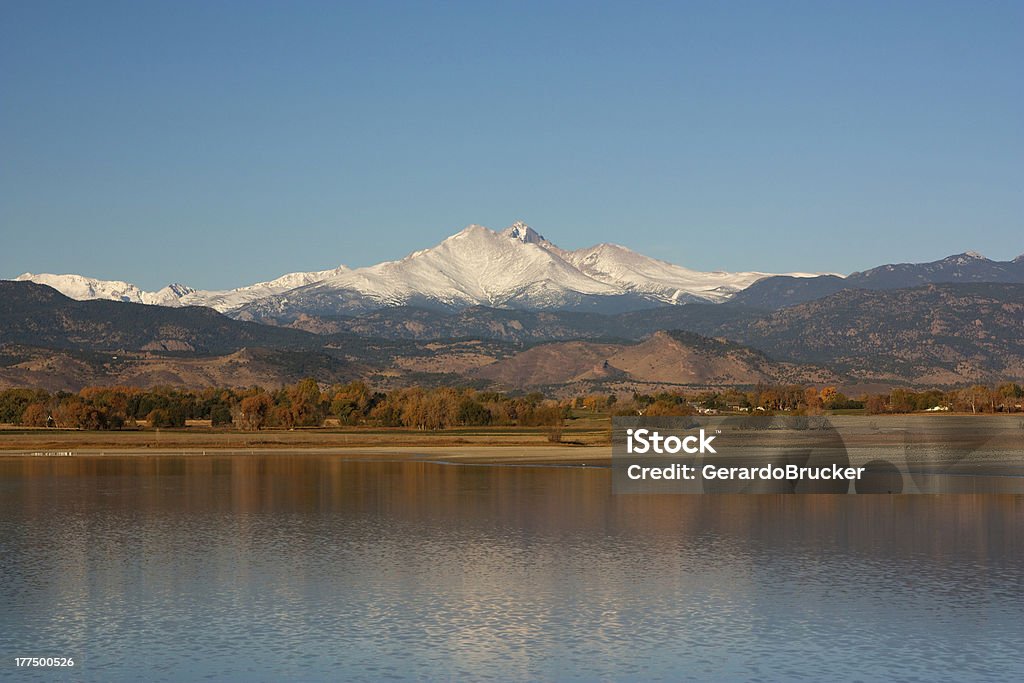 Longs Peak in the Fall from Longmont Colorado "A clear view of Longs Peak and Mount Meeker from Longmont, Colorado and across McIntosh Lake. Clear blue sky, late fall colors on the trees and foliage. A subtle reflection on the water. Horizontal Composition." Autumn Stock Photo