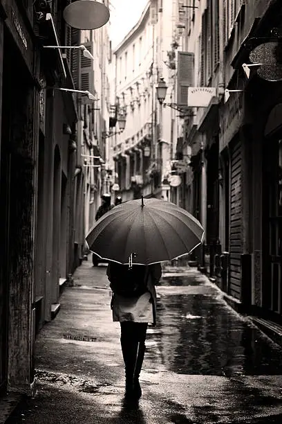 Woman with umbrella in European laneway walking away on rainy day