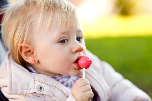 A girl in a park with a lollipop.