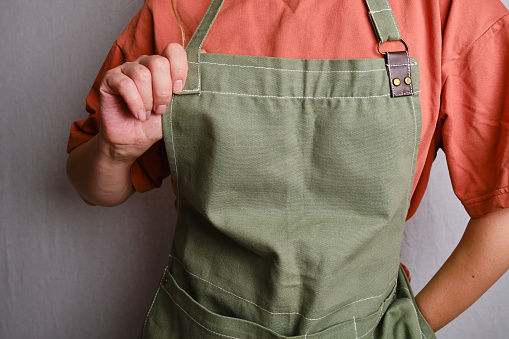 A woman in a kitchen apron. Chef work in the cuisine. Cook in uniform, protection apparel. Job in food service. Professional culinary. Green fabric apron, casual clothing. Handsome baker posing