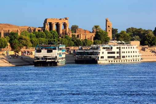 Egypt. Cruise ships docked at Kom Ombo on the Nile. The Temple of Sobek and Haroeris in background - seen colonnade of the Hypostyle Hall