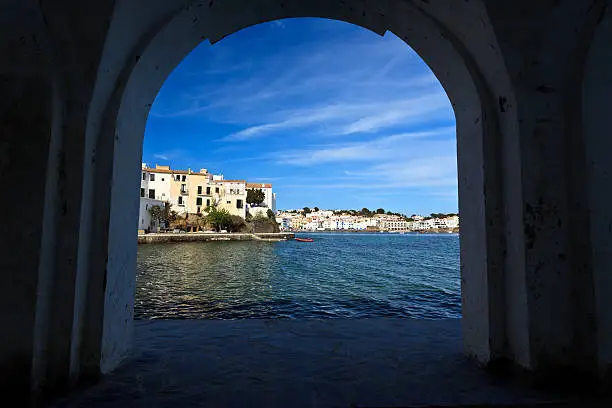 The beautiful Mediterranean fishing village of Cadaques Spain framed by stone arch at the end of the quai.