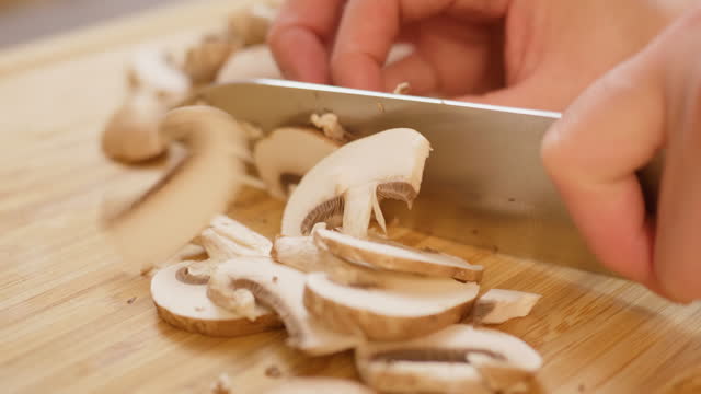 hand chopping mushroom on wooden chopping board