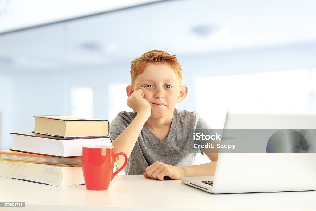 Unhappy young boy with a stack of books Tired bored schoolboy on lesson in classroom Book Stock Photo